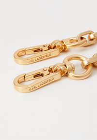 Gullfarget metallkjede med to krok låser og en rund lenke, med "KARL LAGERFELD" gravert på metallbitene for merking.