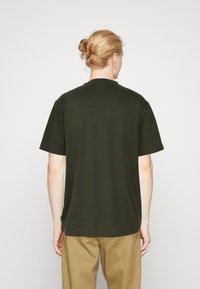 Camiseta de manga corta en verde oscuro, hecha de tela suave, que presenta un diseño clásico de cuello redondo y un dobladillo recto. Sin logotipos ni patrones visibles.