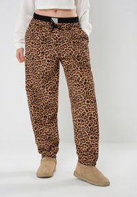 Hlače za trčanje s leopard uzorkom u narančastoj i crnoj boji, s elastičnim pojasom na vezanje, elastičnim manžetama i bočnim džepovima.