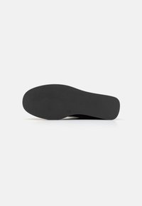Schwarze Gummisohle mit einem strukturierten Muster, leicht abgerundeter Form und glatten Kanten. Robustes Material mit flachem Design.