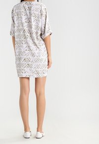 Sukienka z krótkim rękawem o luźnym kroju, z geometrycznym wzorem w białym i jasnoszarym kolorze na miękkim materiale. Długość do połowy uda.