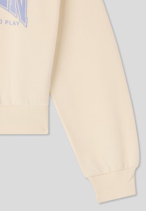 Felpa color crema con polsini a costine, caratterizzata da una vestibilità morbida e una consistenza soffice. Il design include un logo stampato in azzurro chiaro.