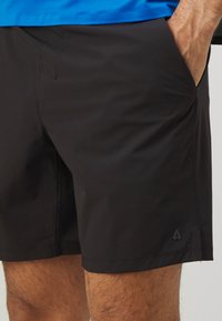 Sorte atletiske shorts lavet af letvægtsstof, med en glat tekstur, skrå sidelommer og et lille logo på kanten.