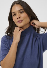 Rövid ujjú, magas nyakú pulóver egyszínű tengerészkék anyagból. Simább textúra, laza fazon, bordázott nyakkal és ujjakkal.