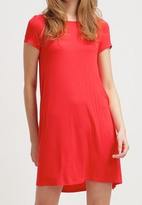 Robe rouge à manches courtes en tissu doux, avec une coupe décontractée, un col rond et un ourlet arrière légèrement plus long. Design simple et polyvalent.