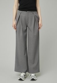 Pantalons larges gris avec un devant plissé, fabriqués en tissu texturé. Associés à des baskets de sport multicolores pour un look décontracté.