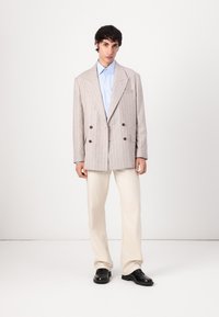 Light gray double-breasted blazer with thin stripes, paired with a light blue shirt and cream-colored trousers. Black shoes.