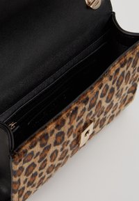 Leopardi-kuvioitu käsilaukku, jossa on musta nahkainen yläosa, kultainen lukko ja pehmeä pinta. Sisäpuolella on vetoketjullinen tasku järjestämistä varten.