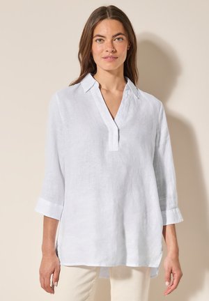 Blouse en lin blanc léger avec une coupe décontractée, col, et manches trois-quarts, présentant un devant sans boutons et des poignets repliés.