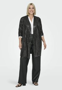 Mustang sequinitega kardigan pikka varrukaga, avatud ette, koos valge pluusi ja mustade nahkpükstega. Vaatamine lõpetatakse mustade kontsaga sandaalidega.