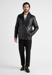 Schwarze Lederjacke mit einem strukturierten, braunen, fellgefütterten Kragen. Verfügt über einen Reißverschluss vorne, zwei Seitentaschen und ein glattes Finish.