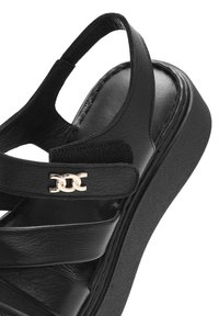 Sandal in pelle nera con fascia incrociata, soletta imbottita e suola a cuneo testurizzata. Include un articolo in catena dorata sulla fascia.