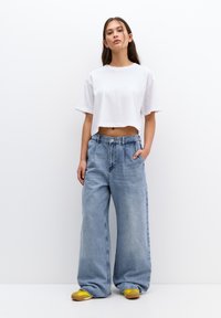 Tricou scurt alb, blugi largi de culoare albastru deschis cu talie înaltă și adidași galbeni. Design minimalist, material moale și croială lejeră.