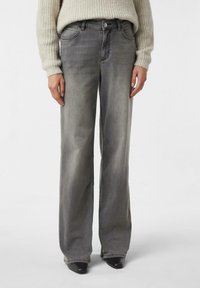 Szare dżinsy o szerokich nogawkach z delikatnym efektem sprania, klasycznym pięciokieszeniowym fasonem, metalowym guzikiem i szlufkami na pasek, zestawione z teksturowanym swetrem z dzianiny.