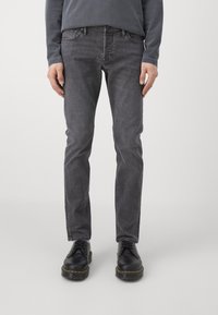 Grå denimjeans med slim fit, fem lommer, synlige sømmer og en lett falmet finish, sammen med svarte snøresko.
