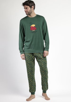 Hombre con camiseta de manga larga verde con el personaje Woodstock y pantalones de pijama verdes con patrón de pequeñas figuras amarillas de Woodstock.