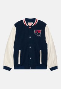 Námořnická modrá univerzitní bunda s krémovými rukávy, žebrovaným límcem, zapínáním na knoflíky, bočními kapsami a vyšívaným logem na levé straně hrudi.