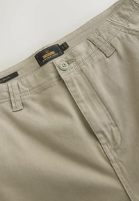 Beige slim-fit bukser med knaplukning, bæltestropper og synlig mærkeetiket "NEXT Durable Goods" i størrelse 34R.