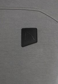 Tessuto grigio con una texture liscia presenta una toppa rettangolare nera con un design testurizzato, posizionata nell'angolo superiore destro.