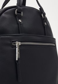 Borsa sintetica nera con forma arrotondata, dotata di una tasca frontale con zip e dettagli in metallo argentato. Texture liscia con cuciture sottili.