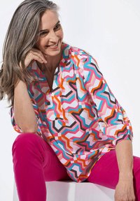 Farbenfrohe, bedruckte Bluse mit geometrischen Formen in Rosa, Orange, Türkis und Schwarz, mit Dreiviertelärmeln und lockerer Passform.