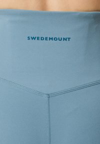 Ljusblå atletiska leggings med en jämn struktur, sömlös design och en synlig logotyp "Swedemount" nära midjan.