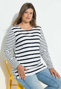 Langärmliges gestreiftes Oberteil in Weiß und Marineblau, mit Rundhalsausschnitt, lockerem Schnitt und Seitenschlitzen, kombiniert mit hellblauen Jeans.