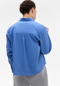 Blue checkered shirt with a button-down collar, long sleeves, and a loose fit. Features contrasting lines in the pattern and a straight hem.