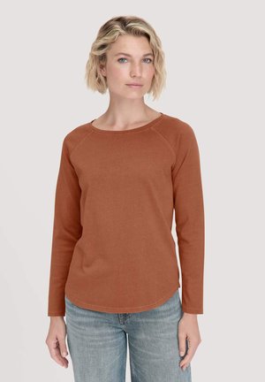 Rostfarbendes Langarmshirt mit geripptem Rundhalsausschnitt und Raglanärmeln. Weiches Material und abgerundeter Saum. Kombiniert mit hellblauer Jeans.