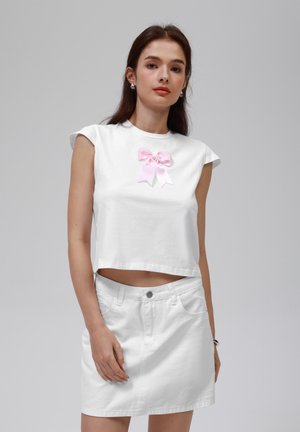 Top corto de algodón blanco con un detalle de lazo de satén rosa en el centro. Combinado con una falda de mezclilla blanca, que presenta un diseño ajustado y bolsillos frontales.
