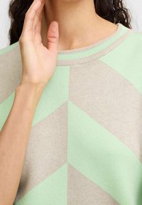 Pull avec un motif géométrique en vert menthe et beige. Fabriqué en tissu doux avec un col rond et des détails côtelés.