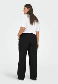 Pantaloni neri su misura con taglio dritto, dotati di tasche laterali e tessuto liscio. Indossati con un top bianco a maniche corte.