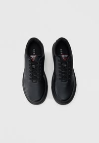 Μαύρο αθλητικό παπούτσι από συνθετικό υλικό με λεία επιφάνεια, υφή μπροστά και πλευρικά πάνελ με σχέδια. Διαθέτει μαύρα κορδόνια και λογότυπο.