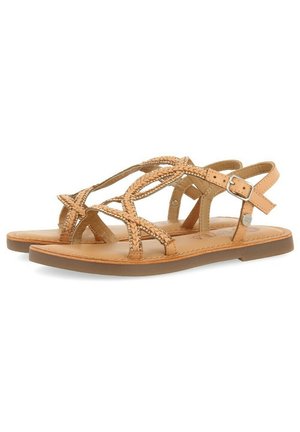Sandales en cuir tan avec des lanières tressées, boucle réglable à la cheville, semelle plate et semelle rembourrée. Présente un design minimaliste et une texture lisse.