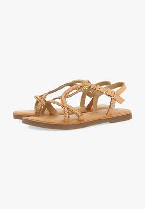 Sandalias de cuero marrón con correas trenzadas, hebilla ajustable en el tobillo, suela plana y plantilla acolchada. Presentan un diseño minimalista y una textura suave.