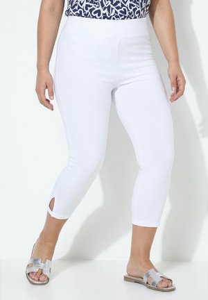 Donna che indossa leggings bianchi corti con spacchi laterali abbinati a sandali piatti argentati aperti in punta e top blu navy con fantasia.
