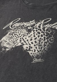 T-shirt noir usé avec un motif imprimé blanc représentant une tête de léopard et le texte "Rewrite Rules" en cursive au-dessus.