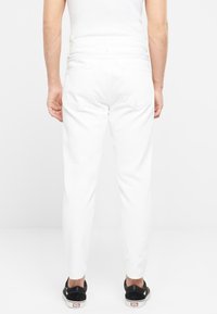 Pantalones de mezclilla blanca con corte ajustado, que cuentan con bolsillos traseros con solapas puntiagudas y una cintura de altura media. Combinados con zapatos de lona negros.
