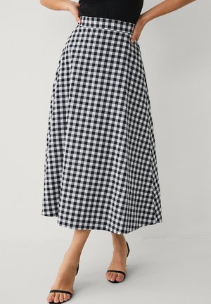 Zwart-witte geruite midi-rok gedragen met zwarte, open sandalen met riempjes en een zwart topje, waarbij de onderlichaam en benen zichtbaar zijn.