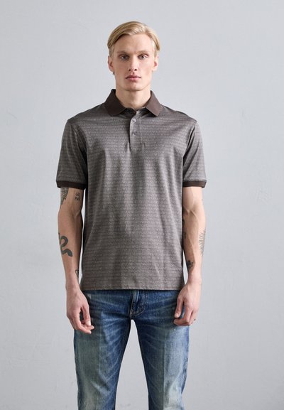 Polo gri cu guler maro, având un model repetat cu logo-uri. Mâneci scurte și croială dreaptă. Asortat cu blugi din denim albastru.