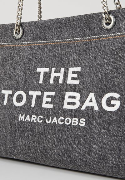 Sac fourre-tout en denim gris avec texte blanc : "LE SAC FOURRE-TOUT" et "MARC JACOBS." Comprend des poignées en chaîne argentées et des coutures orange contrastantes.