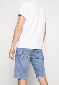 Camiseta de algodón blanca de manga corta combinada con pantalones cortos de mezclilla azul claro que cuentan con dos bolsillos traseros y dobladillos deshilachados.