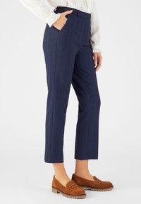 Donkerblauwe, op maat gemaakte broeken met een streeppatroon, voorzien van zijzakken en een hoge tailleband. Gecombineerd met bruine suede loafers.