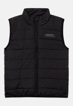 Chaleco sin mangas negro acolchado con cremallera frontal y texto en el pecho "LA AVENTURA ES LA MEJOR MANERA DE APRENDER" en letras pequeñas.