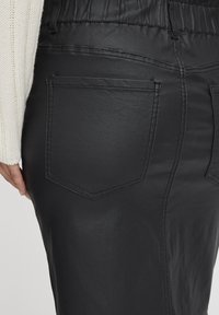 Fustă neagră din piele ecologică cu o textură netedă, talie elastică și două buzunare la spate cu cusături contrastante și un design elegant.