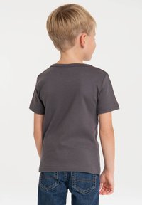 T-shirt grigio a maniche corte in misto cotone, con scollatura rotonda e cuciture ben rifinite, indossato con jeans in denim blu visti da dietro.
