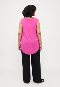 Top senza maniche rosa con orlo curvo, tessuto strutturato e cucitura posteriore sottile, abbinato a pantaloni larghi neri e scarpe basse.