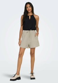 Black sleeveless top with a keyhole neckline, beige textured shorts with an elastic waistband, and beige lace-up shoes with a thick sole.