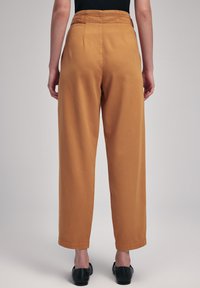 Wijd-pijpenbroek in mosterdgeel, met een hoge taille en een gladde textuur, afgewerkt met opgerolde boorden, gecombineerd met zwarte schoenen.
