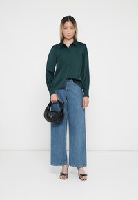 Grønn sateng knappeskjorte, vide blå jeans, svart håndveske og mønstrede sandaler med sløyfer. Enkel design og teksturerte materialer.